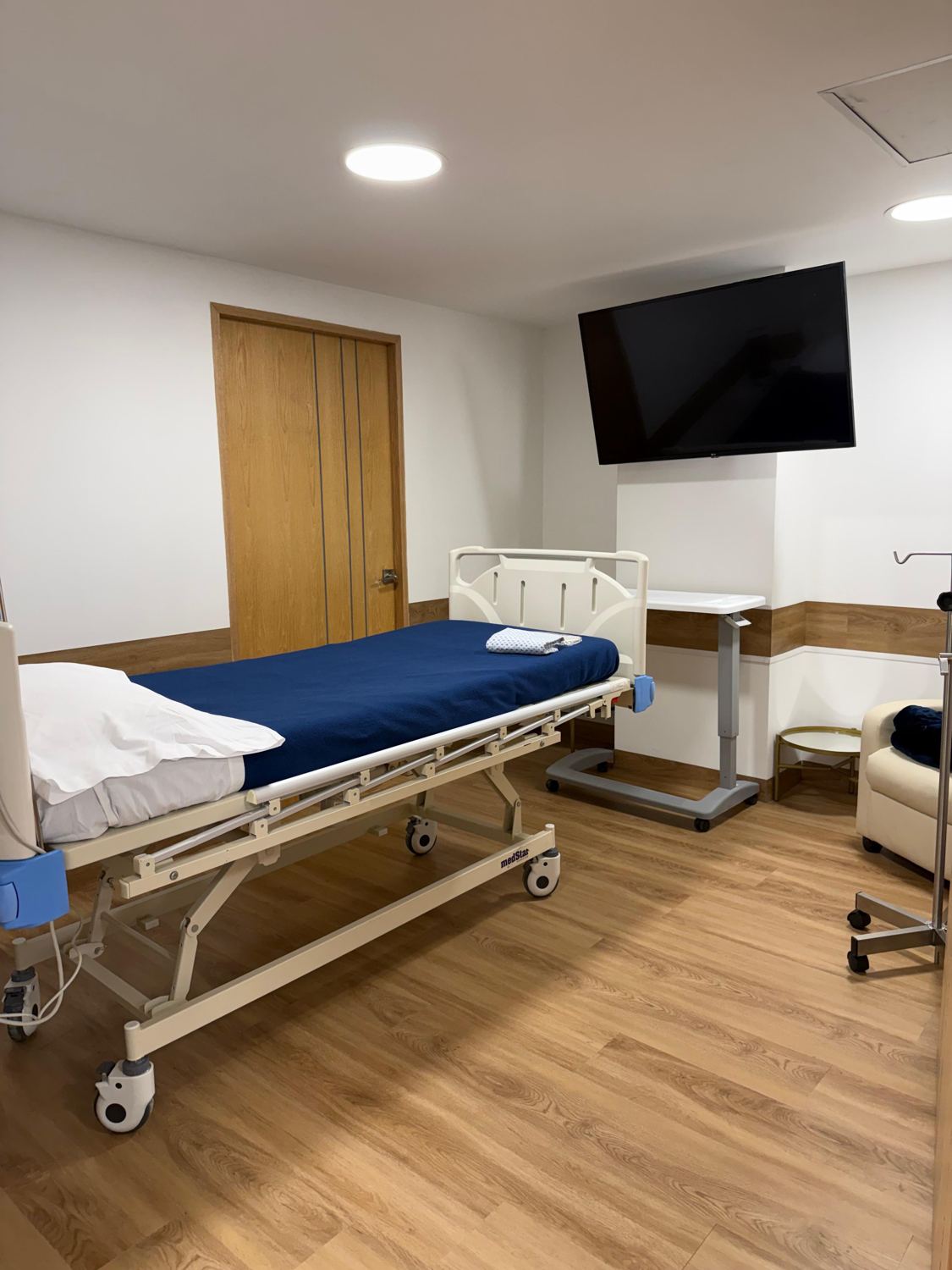 Habitación de paciente con cama hospitalaria, puerta de madera y guardasilla de madera en los muros